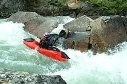 A kayaker paddling through whitewater between boulders